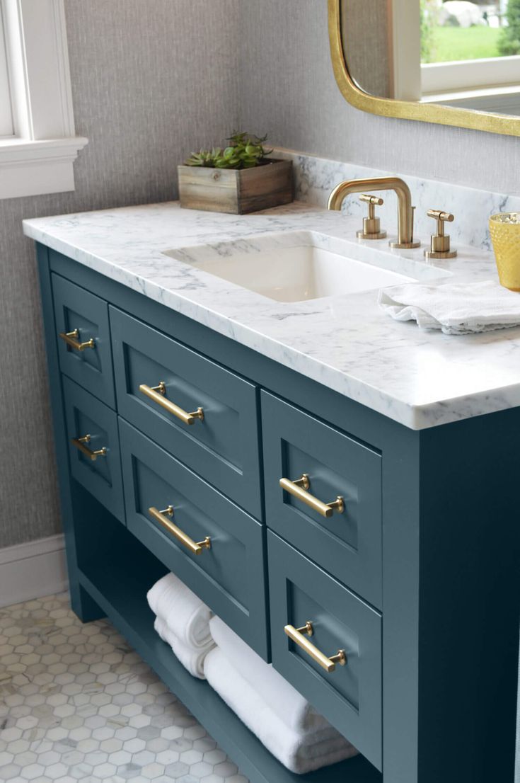 a bathroom vanity with marble counter top and gold faucet pulls on the sink