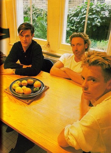 three men sitting at a table with oranges on the plate in front of them