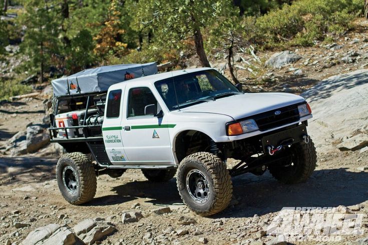 a white truck driving down a dirt road next to rocks and trees on the side of a hill