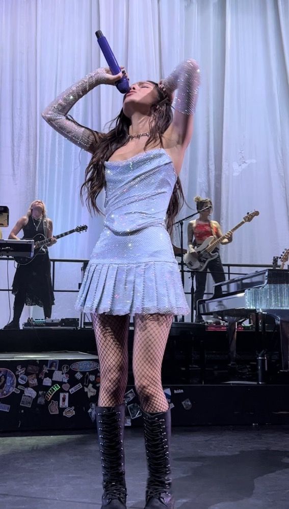 a woman in a short dress and boots on stage with her hands behind her head