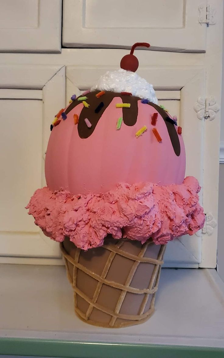 an ice cream cone with pink icing and sprinkles on it sitting in front of a white cabinet