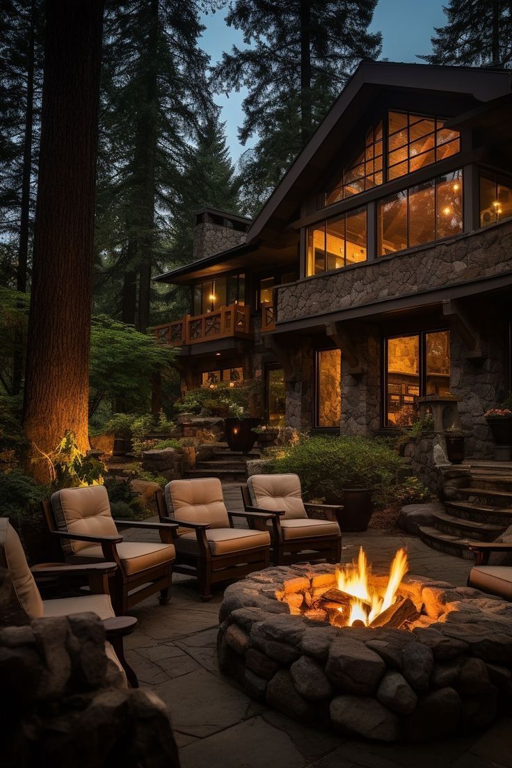 a fire pit sitting in front of a large house with lots of windows and chairs around it