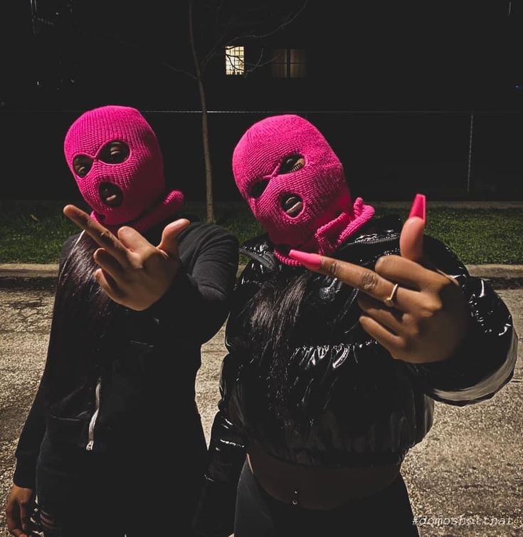 two women in pink knitted masks pointing fingers at the camera