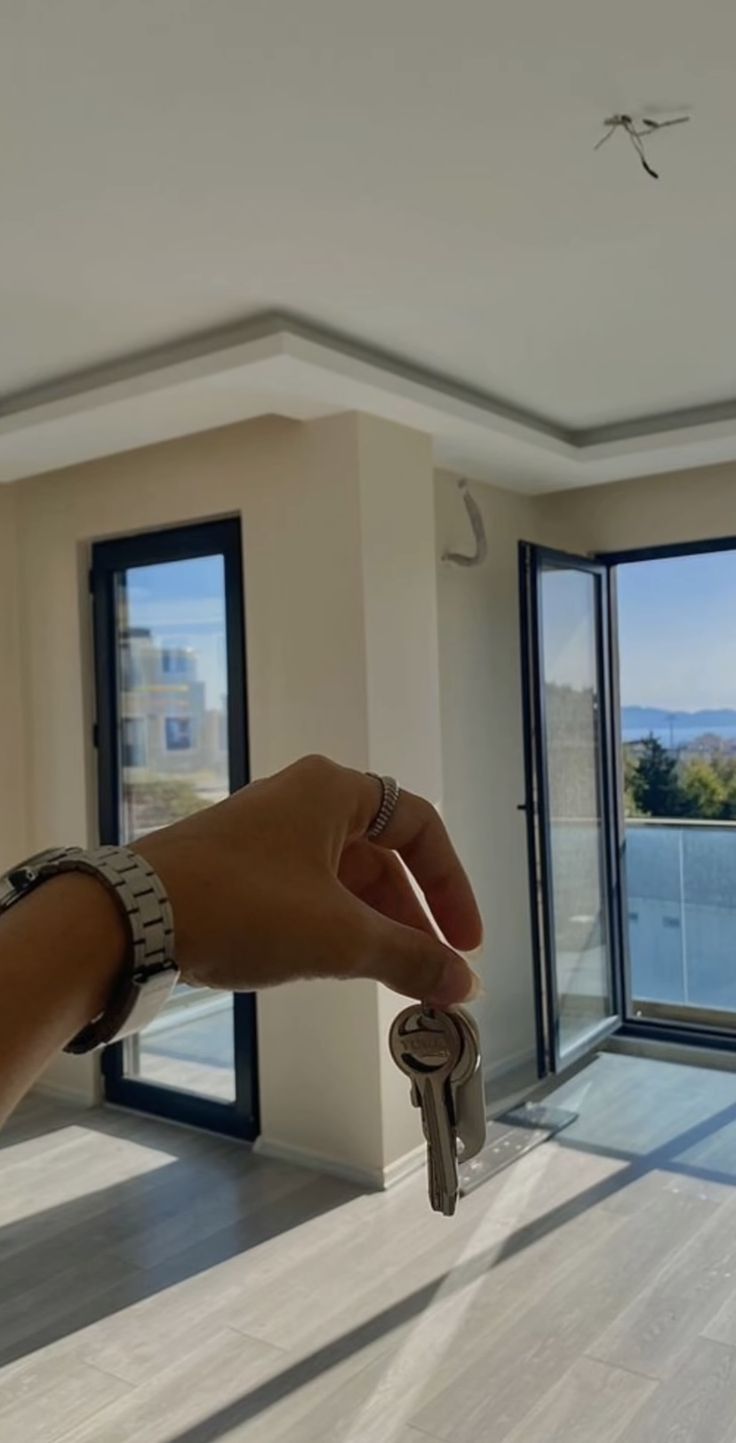 a hand holding a key in front of an open window with the view of water