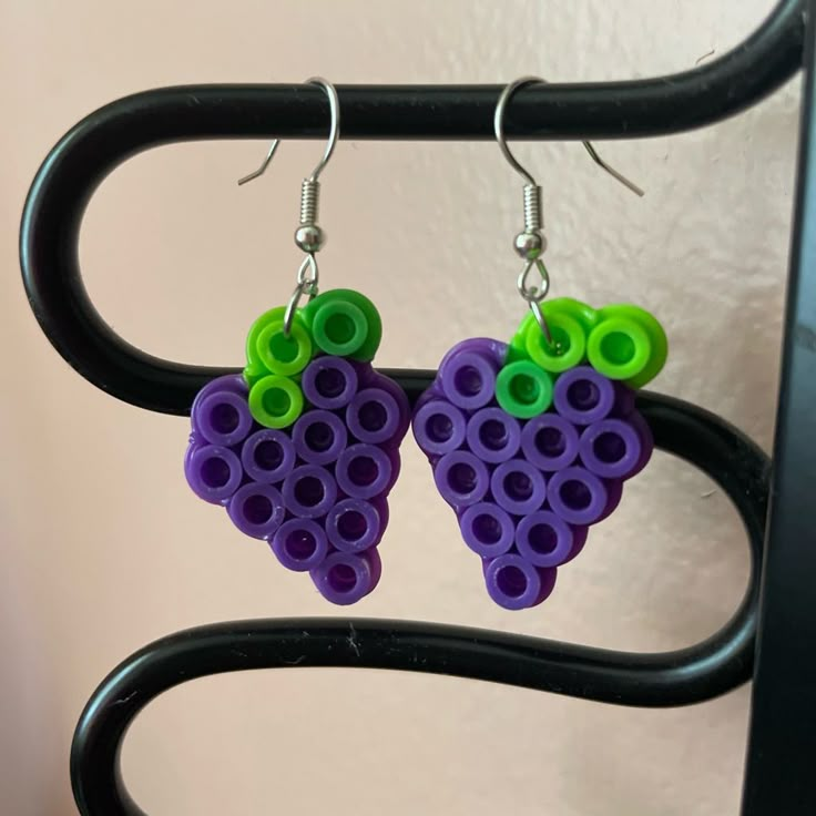 two purple and green grapes shaped earrings on a black rack with metal hooks hanging from it's earwires