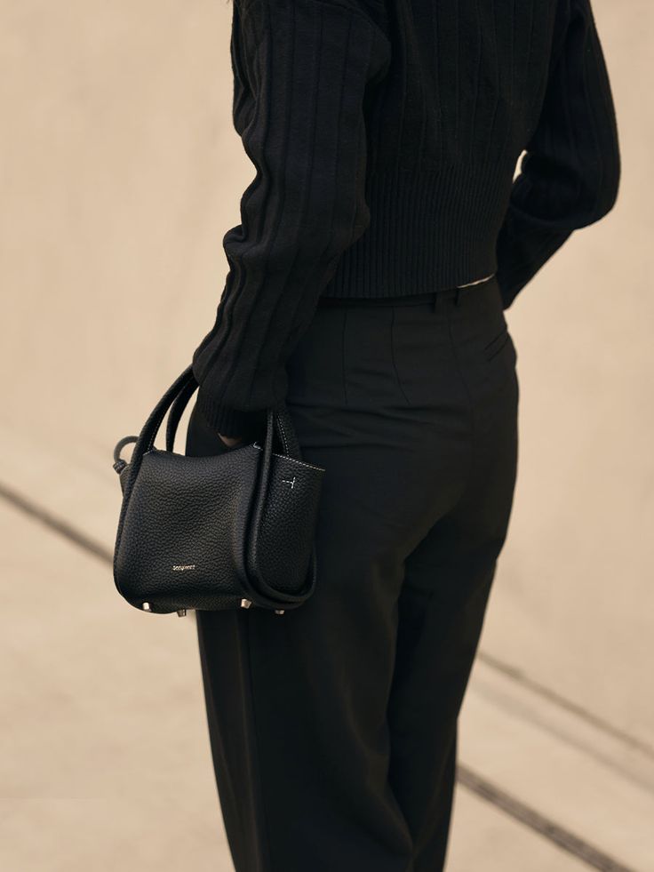 a woman in black is holding a handbag