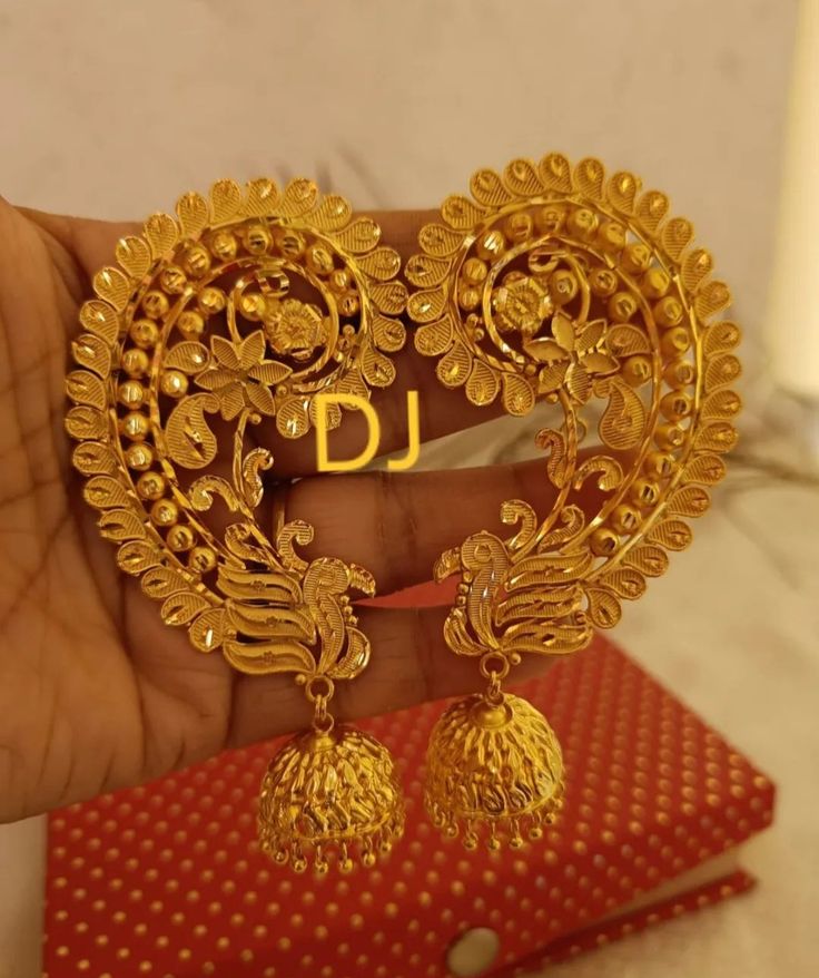 a pair of gold earrings with the letter j on it in front of a red box