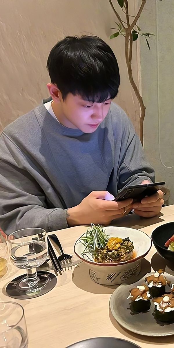 a young man sitting at a table looking at his cell phone while eating sushi