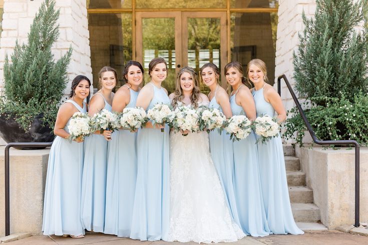 a group of women standing next to each other in front of a building holding bouquets