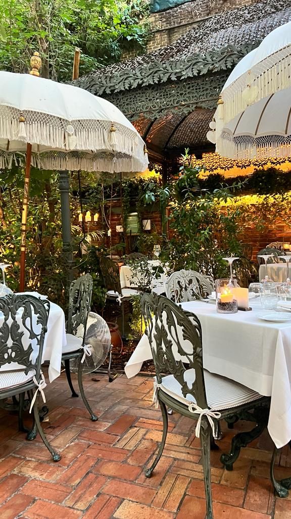 an outdoor dining area with tables and chairs covered in white tablecloths, lit by candles