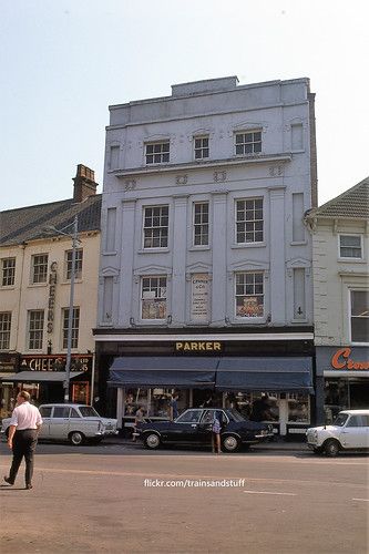 a man walking down the street in front of a building with cars parked on it