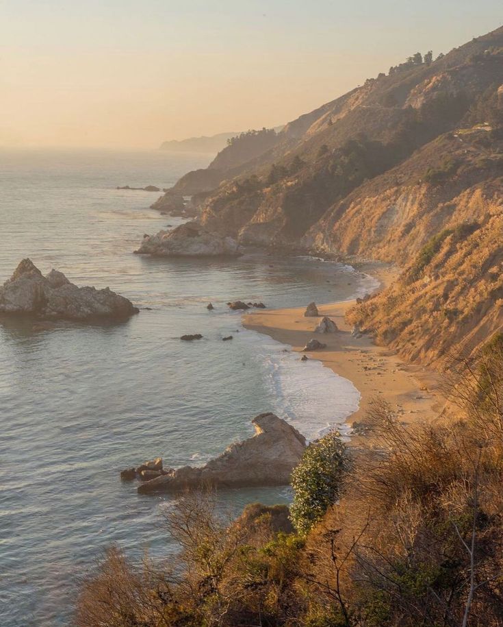 an ocean view with rocks in the foreground and trees on the other side, at sunset