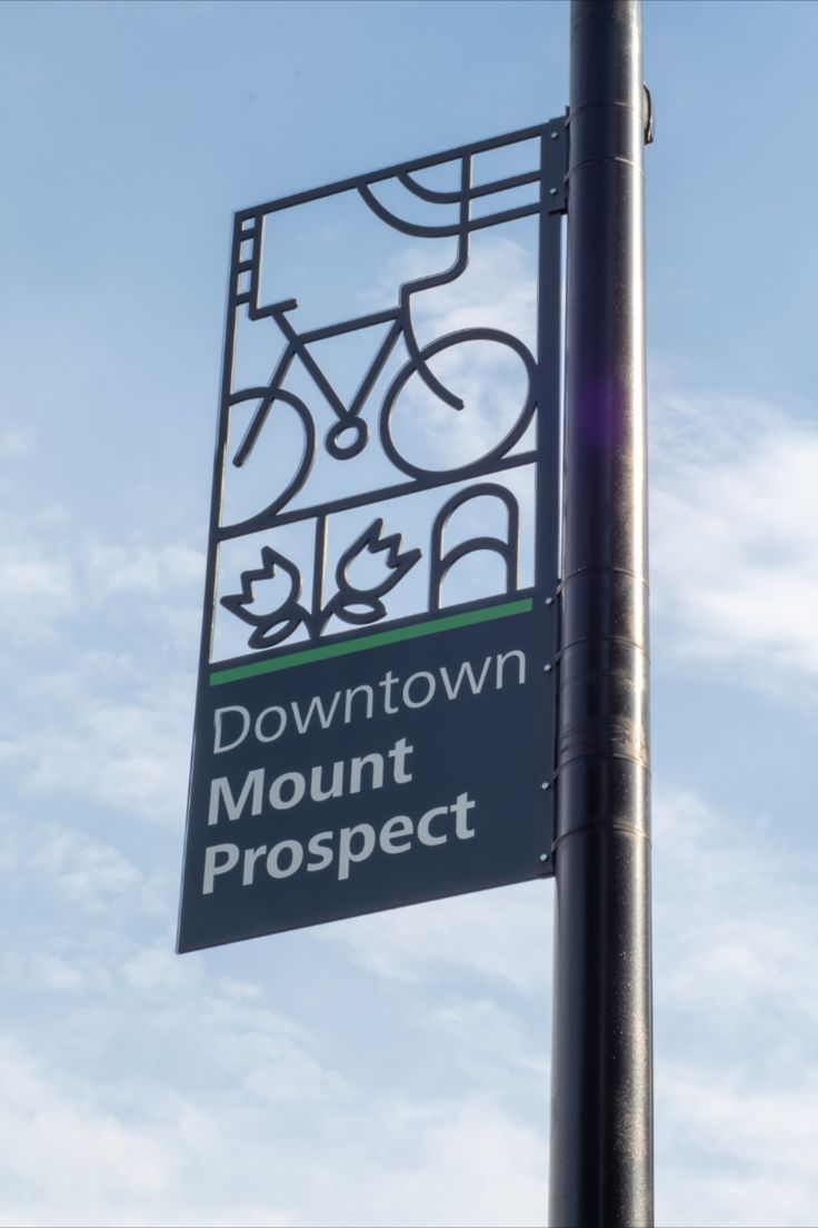 a street sign that reads downtown mount prospect on the side of a metal pole in front of a blue sky with wispy clouds