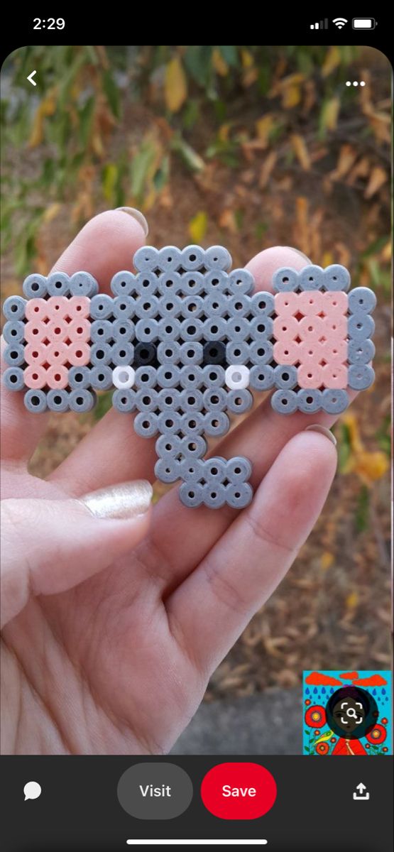 a person holding up a small beaded object in their hand with the image of an elephant on it's face