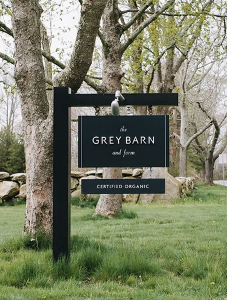 the grey barn and farm sign in front of some trees