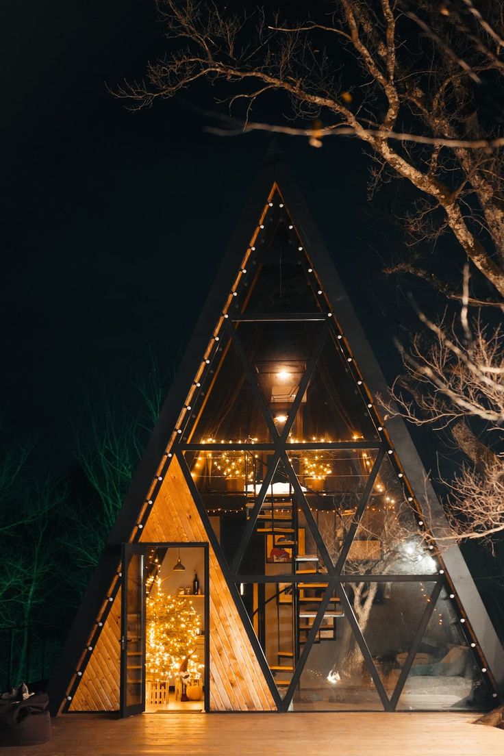 a wooden structure with lights on the outside and inside it at night, in front of some bare trees