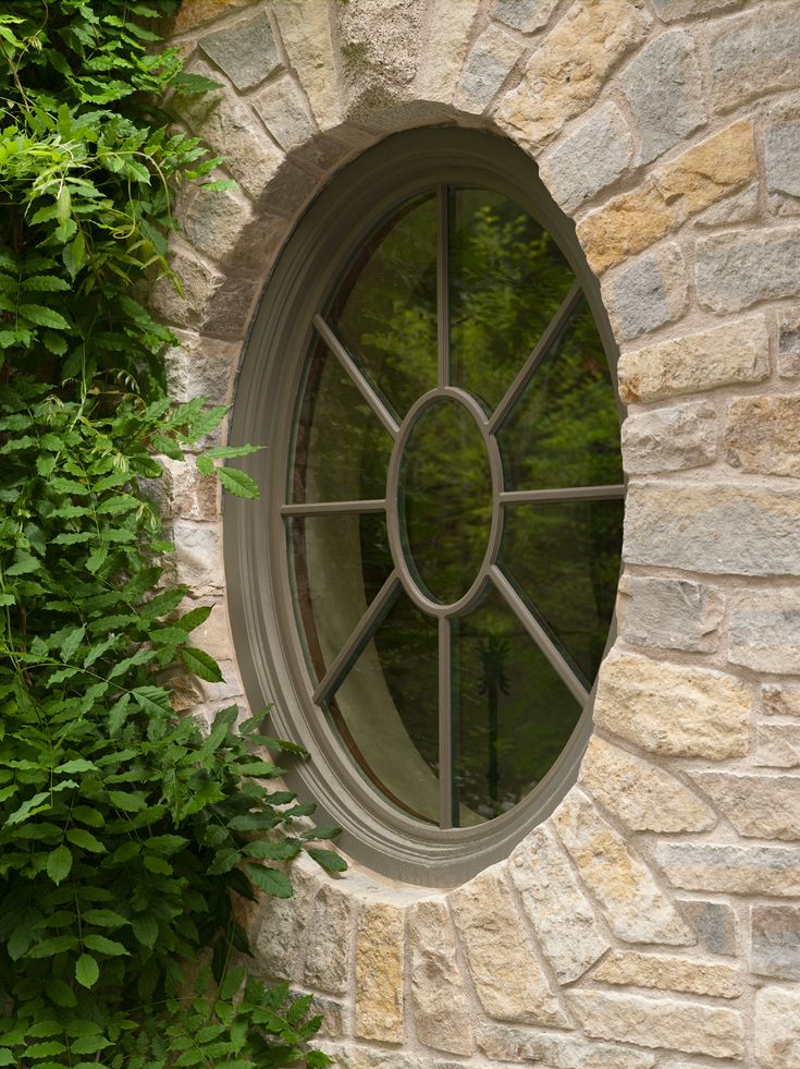 a round window on the side of a stone building with greenery around it and an arched glass door