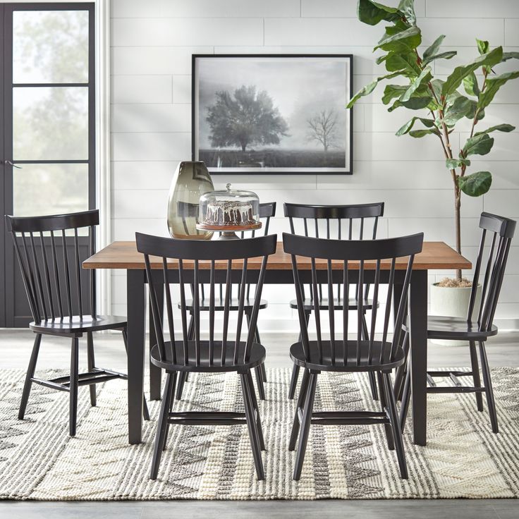 a dining room table with black chairs and a potted plant on the rug in front of it