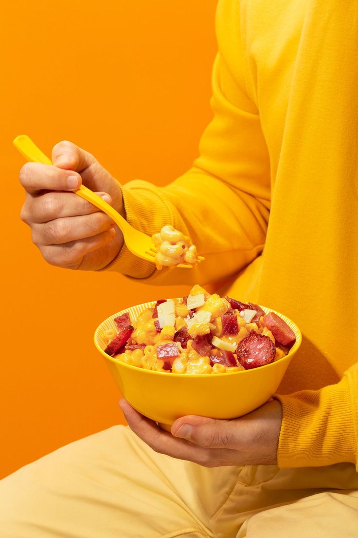 a man is holding a bowl of fruit and a spoon in his hand while sitting down