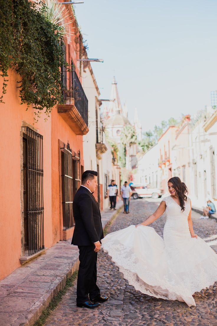 a bride and groom are walking down the street in their wedding attire, holding each other's hands