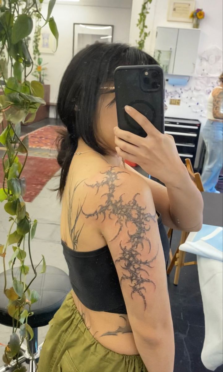 a woman taking a selfie with her cell phone in front of her back tattoo