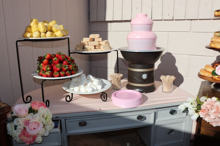 a table topped with lots of desserts and pastries next to a wall covered in flowers