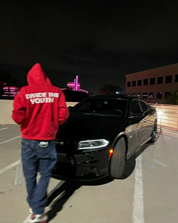 a man in a red hoodie standing next to a black car