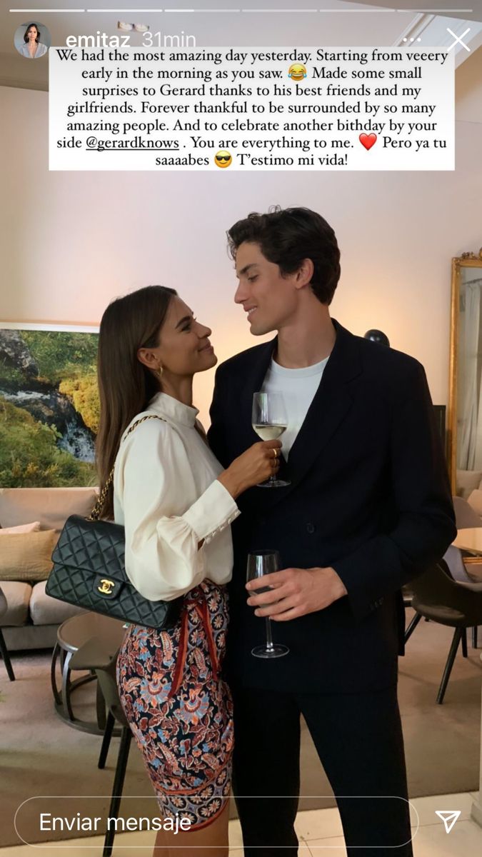 a man and woman standing next to each other with wine glasses in their hands, looking at each other