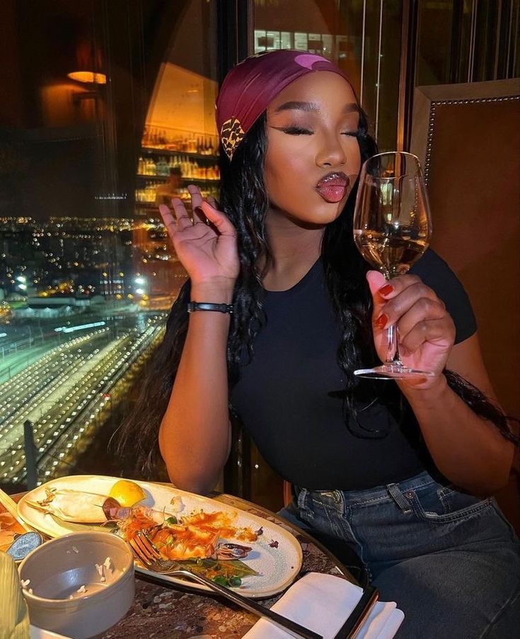 a woman sitting at a table with a glass of wine in her hand and food on the plate