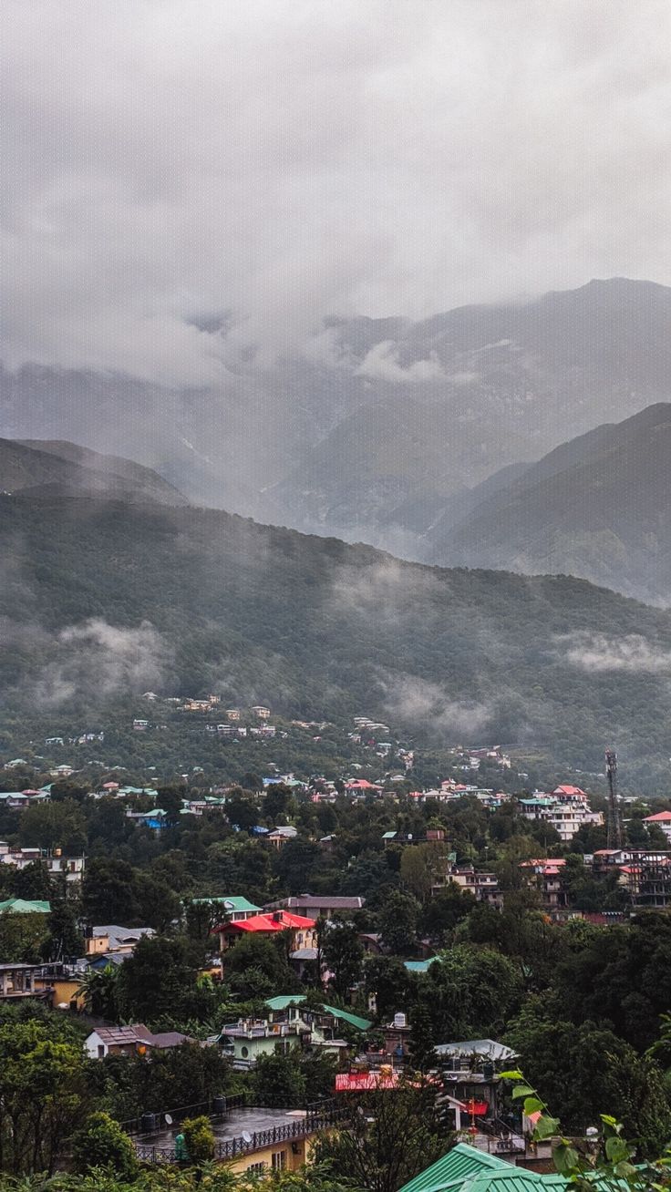 a city with mountains in the background and houses on the hillsides below, under cloudy skies