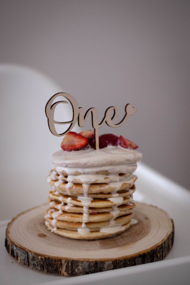 a stack of pancakes with white frosting and strawberries on top that say one