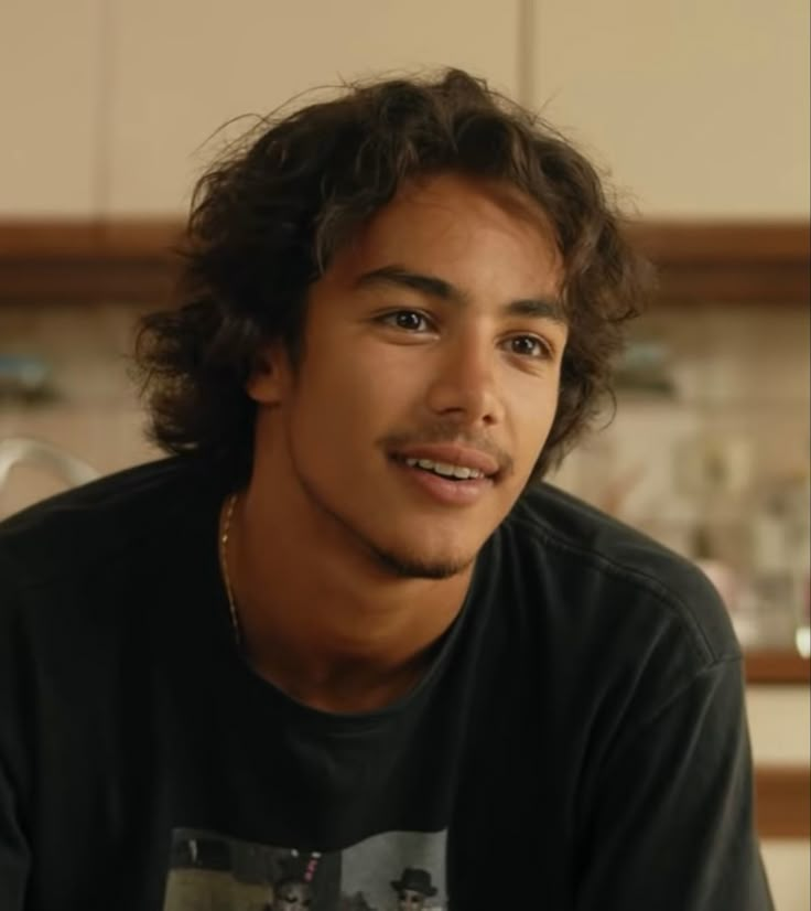 a young man with curly hair sitting in a kitchen