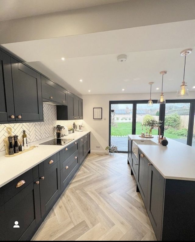 a large kitchen with wooden floors and gray cabinets, white counter tops and wood flooring