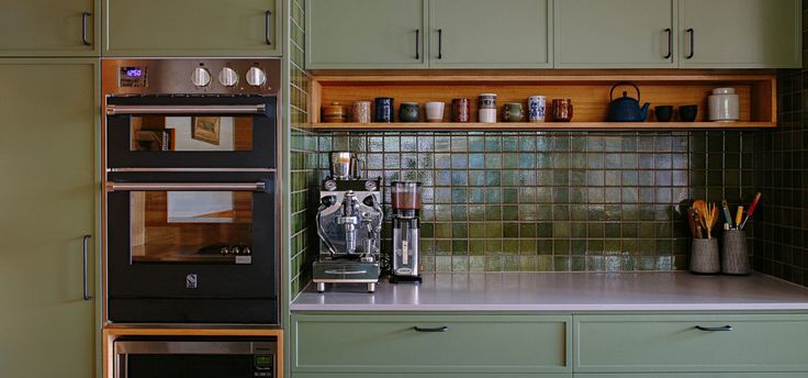 a kitchen with green cabinets and an oven in the middle, next to a coffee maker