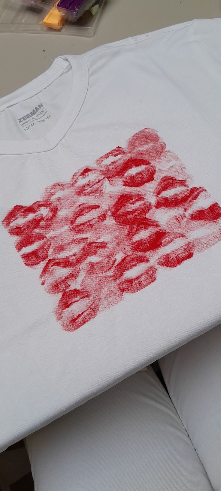 a white t - shirt with red lipstick prints on the front and back, sitting on a table