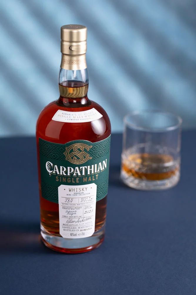 a bottle of carpathhan single malk whisky next to a glass on a table