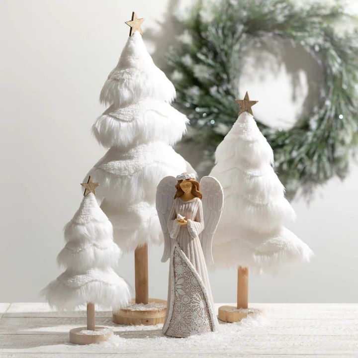 an angel figurine standing in front of three white christmas trees with gold stars