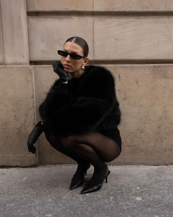 a woman in black is squatting on the ground with her legs crossed and wearing high heeled shoes