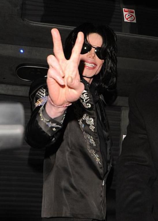 the man is wearing a black suit and holding up his peace sign