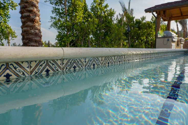 an outdoor swimming pool with palm trees and blue tiles on the edge, in front of a gazebo