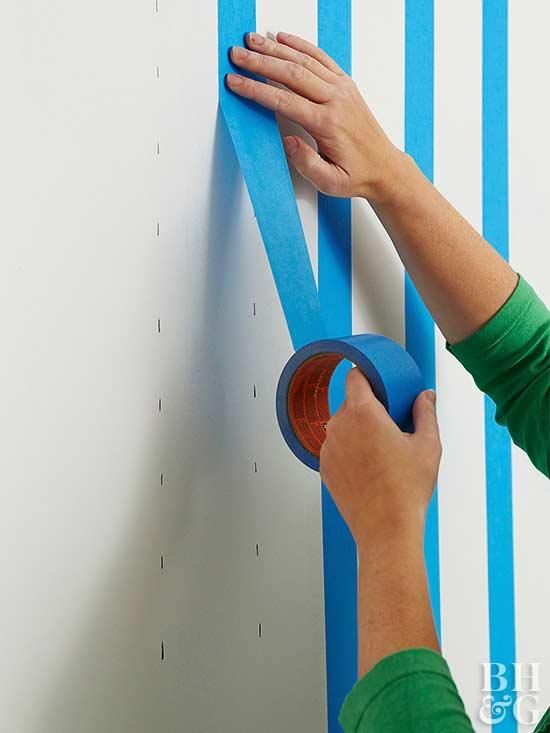 a person is using tape to decorate a wall with blue stripes on it and another hand reaching for the tape