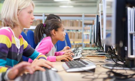 several children are sitting at computers in a library and one is using the computer keyboard