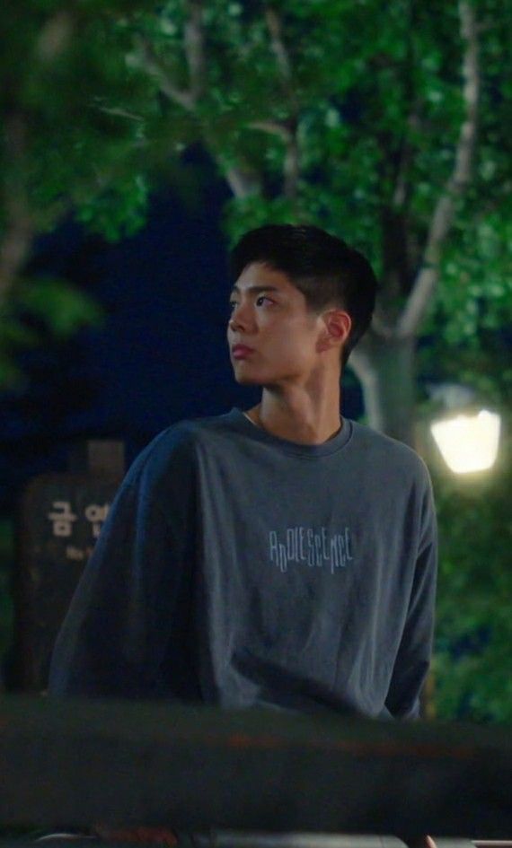 a young man standing in front of a tree at night looking off into the distance