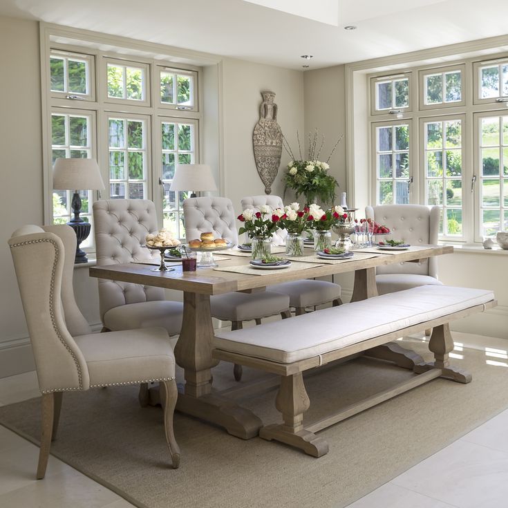 a dining room table and chairs in front of large windows with vases on them