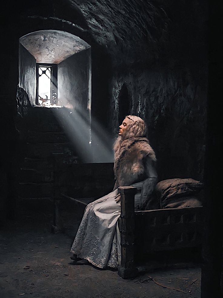 a woman sitting on a bed in a dark room with light coming through the window