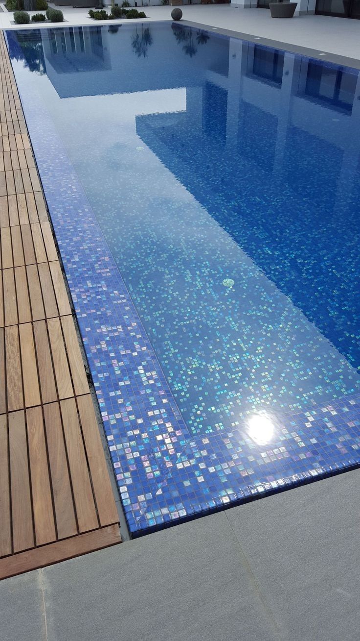 an empty swimming pool with wooden decking and blue tiles on the side, in front of a building