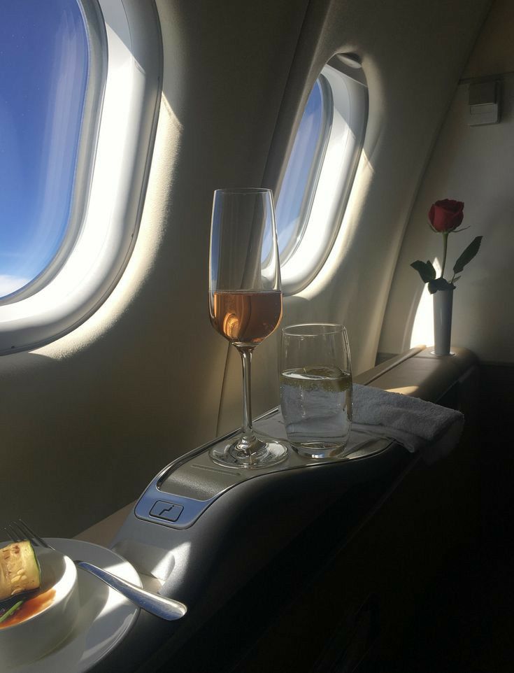 a glass of wine and some food on a tray in front of an airplane window