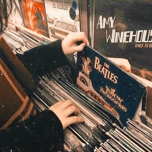 a person holding up a record player in front of a rack of records at a store