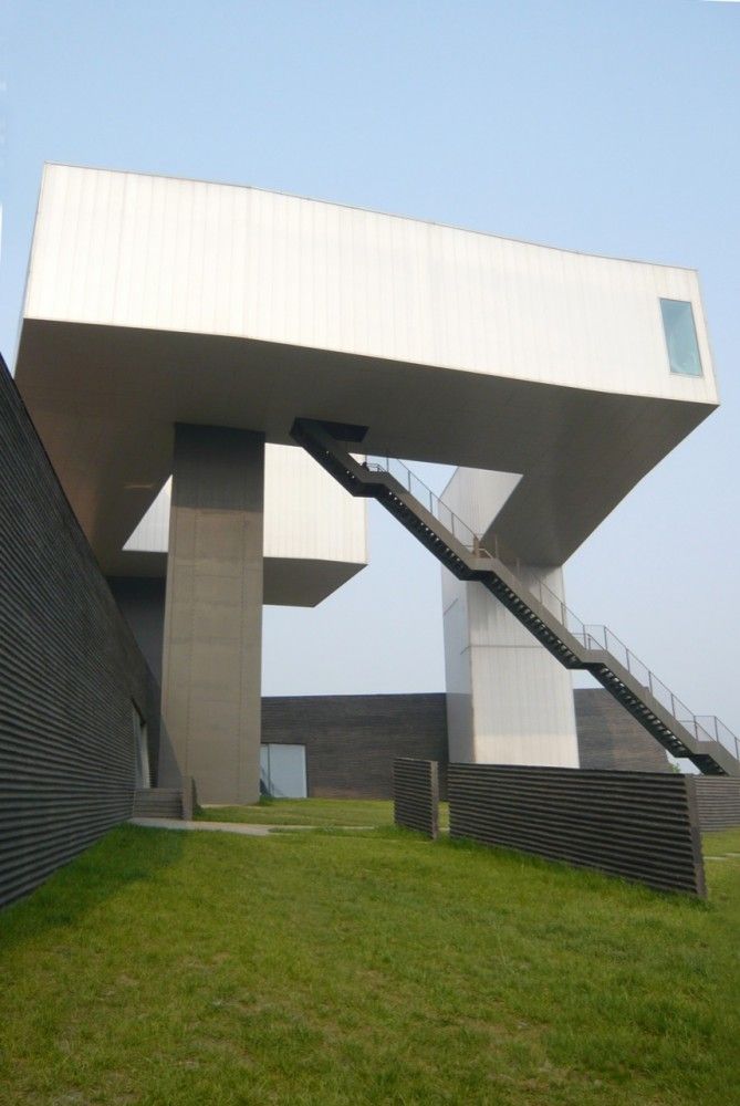 an unusual building with stairs leading up to it's roof and grass area in front