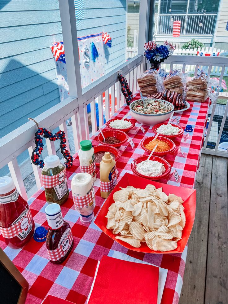 a red and white checkered table cloth with food on it sitting on a porch